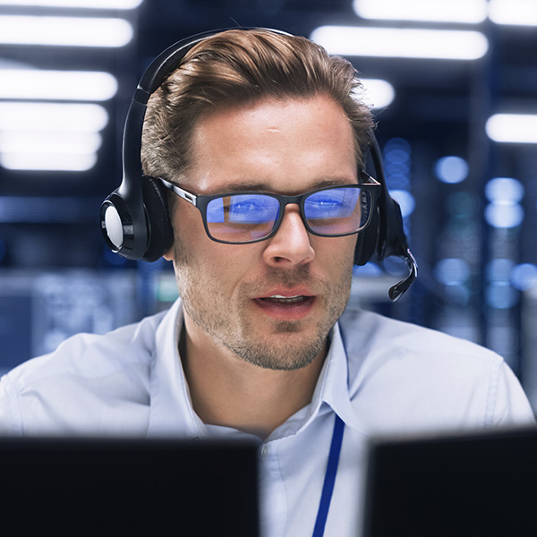 Um homem com fones de ouvido, microfone e óculos olhando para uma tela com concentração, simbolizando o serviço ao cliente responsivo e profissional da Teldar Connect.